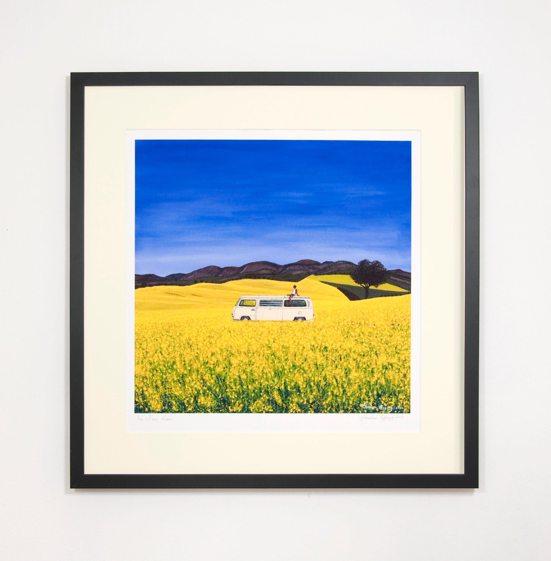 Beautifully framed high quality giclee print of free roam, a man sitting on the roof of a white campervan on a sunny day of blue skies in yellow flower fields with trees and hills in the background. Contemporary high quality affordable art prints.